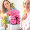 Eine Frau hält einen Strauß rosa Rosen und eine pinke Rosenbären-Geschenkbox.
