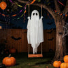 A white ghost decoration hangs from a tree branch in a dark outdoor Halloween setting with pumpkins and bats.