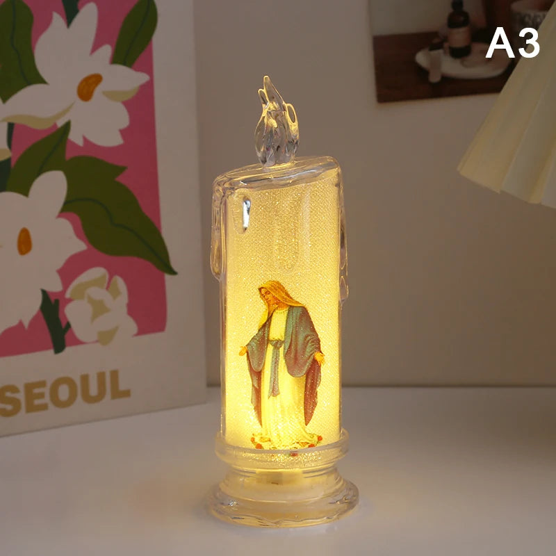 A clear glass flameless LED religious prayer candle with a golden figure inside, set on a white surface.