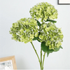 A cluster of artificial light green hydrangea flowers on a green stem against a white background.