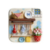 A white ceramic tray holds a woven basket, various kitchen utensils, and small decorative items on a light blue background.