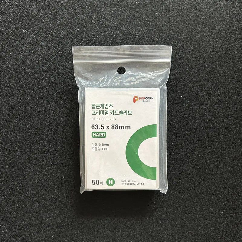 A package of 50 Crystal Clear Protective Card Sleeves with a green 'C' logo is shown on a dark surface.