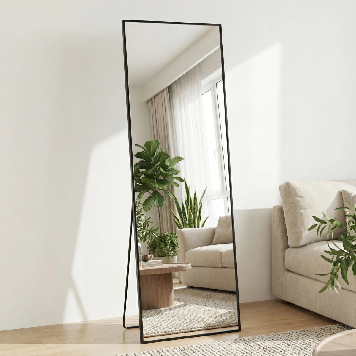 A tall, rectangular floor mirror with a black frame reflects a bright room and green plants.