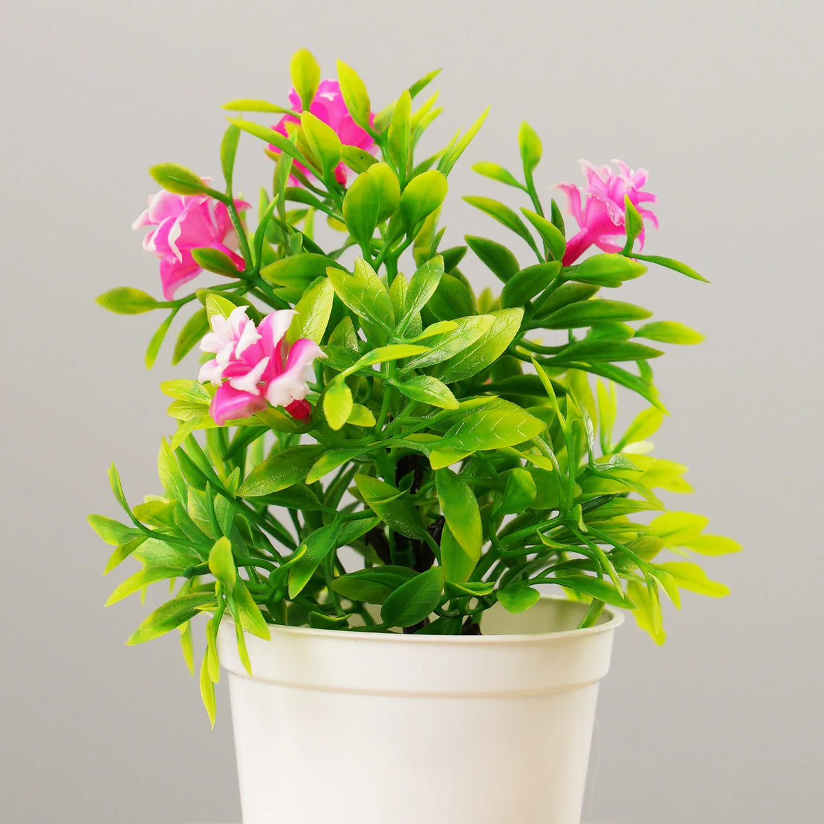 A vibrant artificial bonsai tree with bright pink and green leaves in a white pot.
