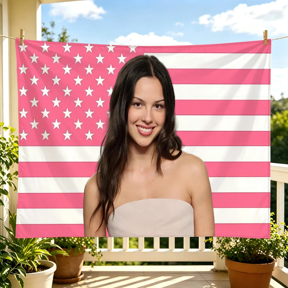 A young woman smiling while holding a pink and white American flag tapestry in an outdoor setting.