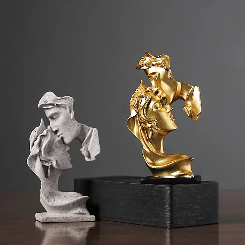 Une paire de statues en résine dorée représentant des amants s'étreignant, présentées sur une base en bois noir.