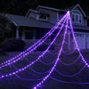 Purple string lights shaped like a spider web draped across a lawn in front of a house at night
