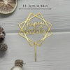 A gold acrylic cake topper shaped like a geometric star with the words Happy Birthday on a stick.