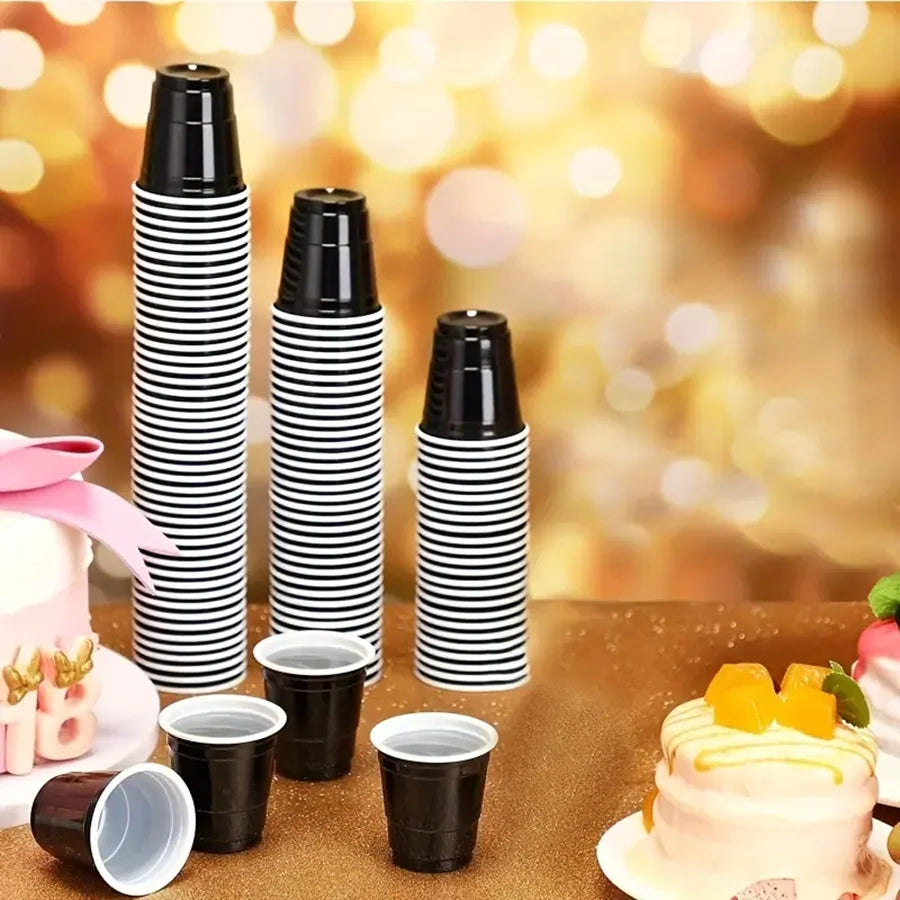 A display of black and white striped mini plastic shot cups for tastings and parties on a brown surface.