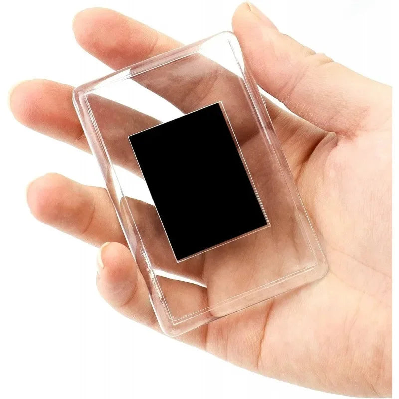 A clear square photo frame magnet with a black insert is held in a person's hand.