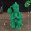 A small green resin figurine of Hanuman, a Hindu monkey god, sitting in a prayer pose.