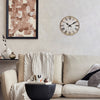A round wooden wall clock with Roman numerals hangs on a light-colored wall above a beige sofa.