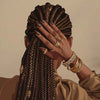 A portrait of a woman with braided hair and gold jewelry, shown from the back, against a neutral background.