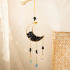 A handcrafted gold moon crystal suncatcher with a black crescent pendant and dangling prism charms.
