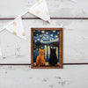 A wooden art print depicting two cats silhouetted against a starry night sky and water.
