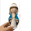 A handcrafted crochet doll of the Virgin Mary with a white crown and blue garment being held in a hand.