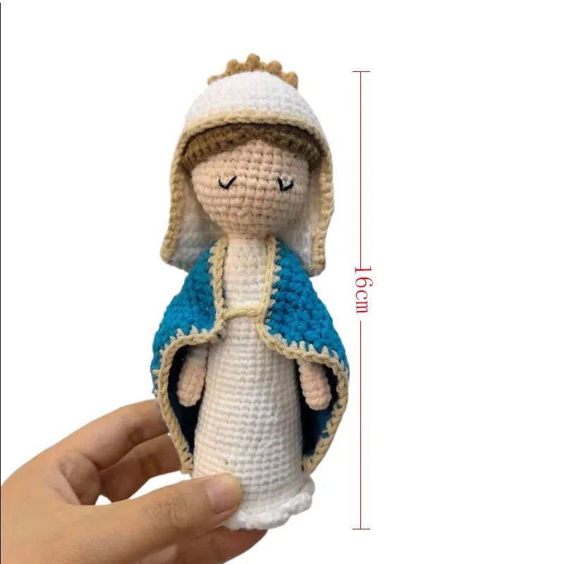 A handcrafted crochet doll of the Virgin Mary with a white crown and blue garment being held in a hand.
