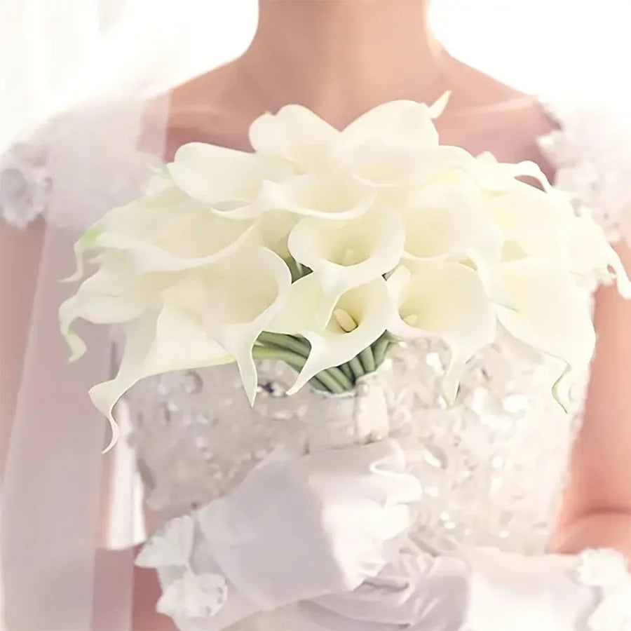 A close-up of white calla lily flowers arranged in a bouquet, held by a person.