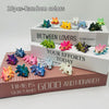 A collection of ten random colored articulated baby dragon figurines displayed on a wooden box.