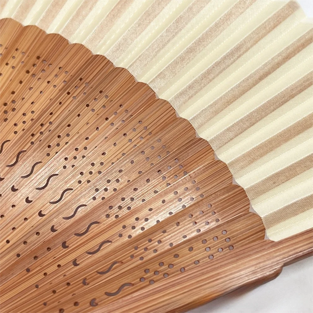 A close-up of an elegant bamboo folding fan with a classic design showing fine perforations and natural wood grain.