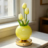 A yellow glass vase holds three white tulips on a gold base, illuminated by a soft light.