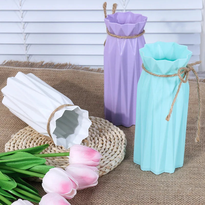 A purple plastic vase with a basket design stands next to a light blue plastic vase and pink tulips on a burlap surface.