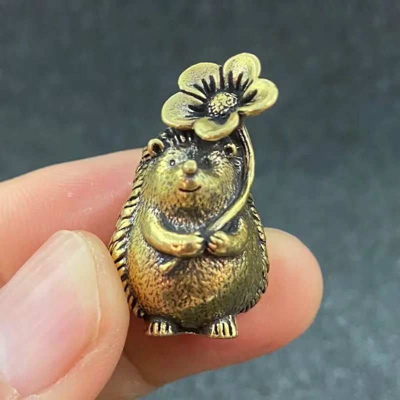 A small brass figurine of a hedgehog with a leaf and flower detail, held in a hand.