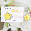 A card with a star drawing and text encouraging someone to be a star, next to a yellow star keychain.