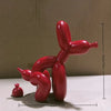 A bright red, abstract sculpture of a dog in a squatting pose, made from inflated balloons.