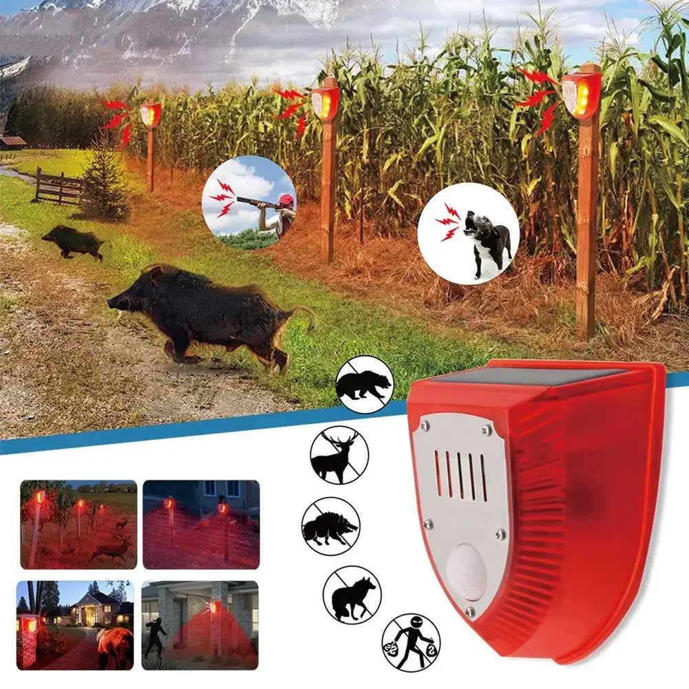 A red solar-powered motion sensor alarm with a flashing siren is shown outdoors in a field setting.