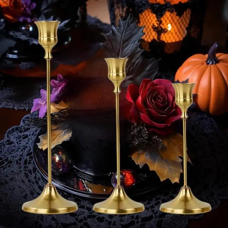 A set of three ornate vintage gold metal candle holders displayed on a black lace tablecloth with autumn foliage and pumpkins