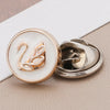 A close-up of a gold-toned pearl and rhinestone no-sew brooch button featuring a stylized swan design.