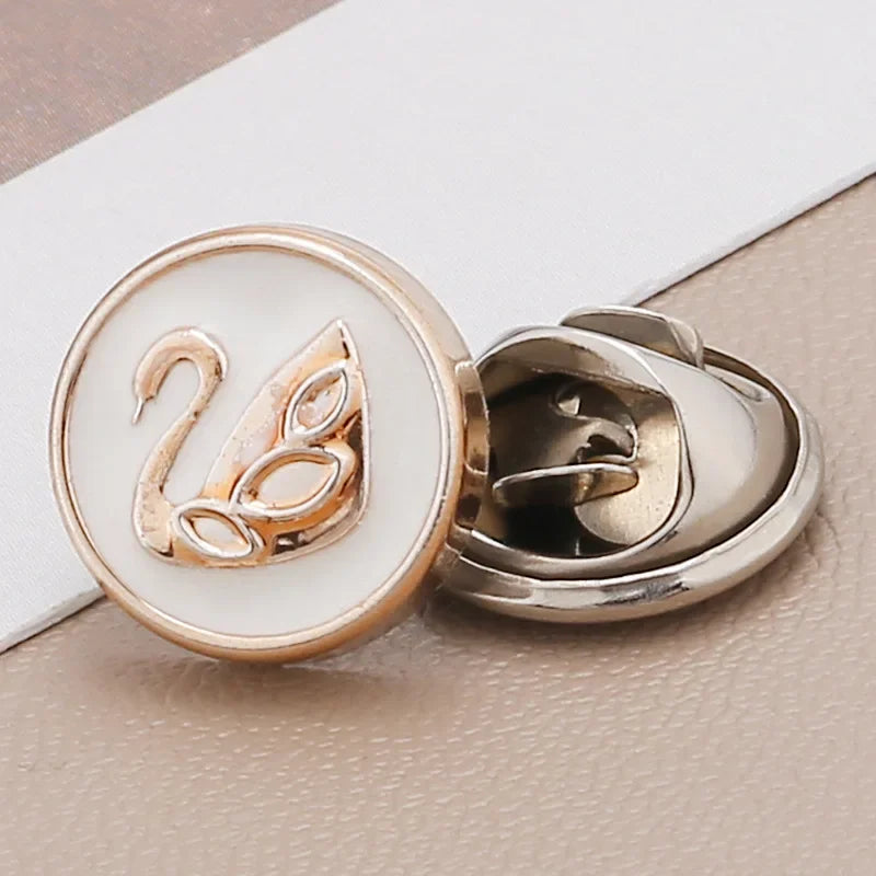 A close-up of a gold-toned pearl and rhinestone no-sew brooch button featuring a stylized swan design.