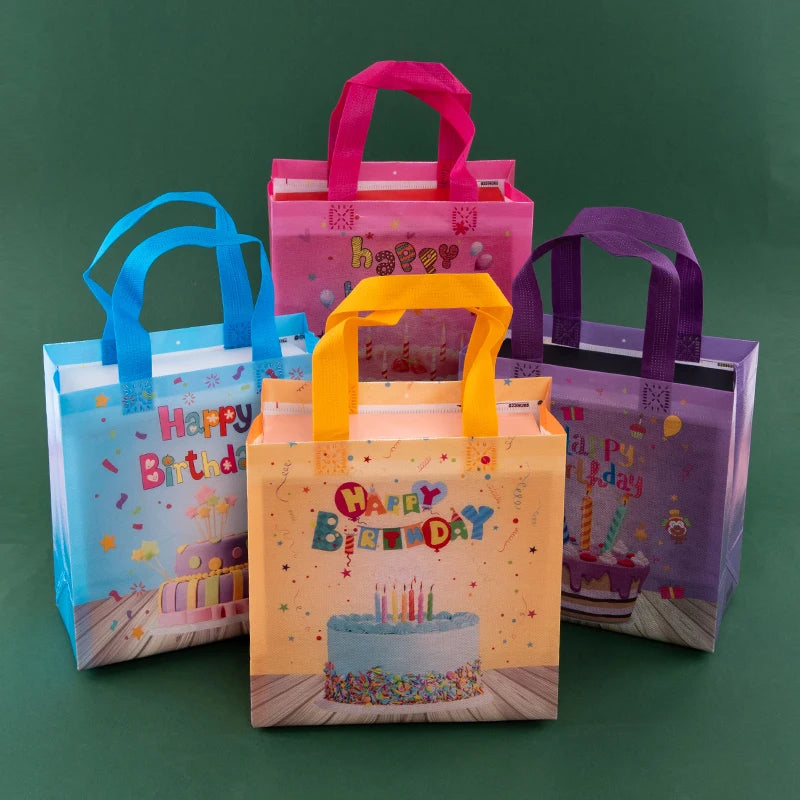 A set of colorful reusable happy birthday gift bags in pink, orange, and purple are displayed on a green surface.