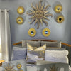 A set of three gold sunflower wall mirrors mounted on a gray wall above a wooden bed.