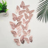 A set of twelve pink and brown 3D butterfly wall stickers arranged on a white surface next to a potted plant.