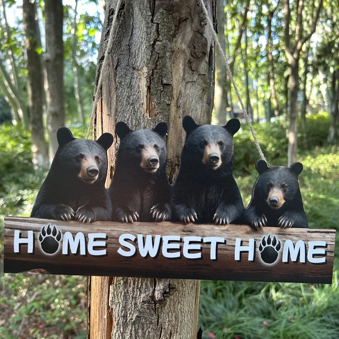 Four black bear cubs sit on a rustic wooden sign that reads Home Sweet Home hanging from a tree.
