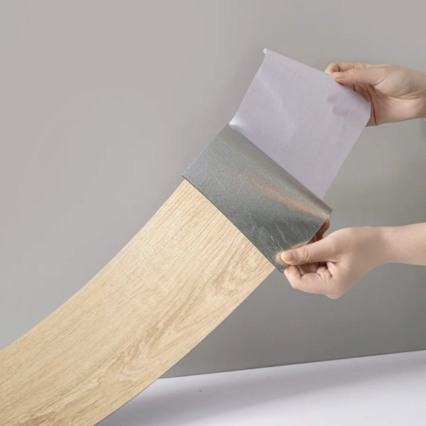 Hands peel a sheet of wood grain peel-and-stick floor and wall stickers from a roll.