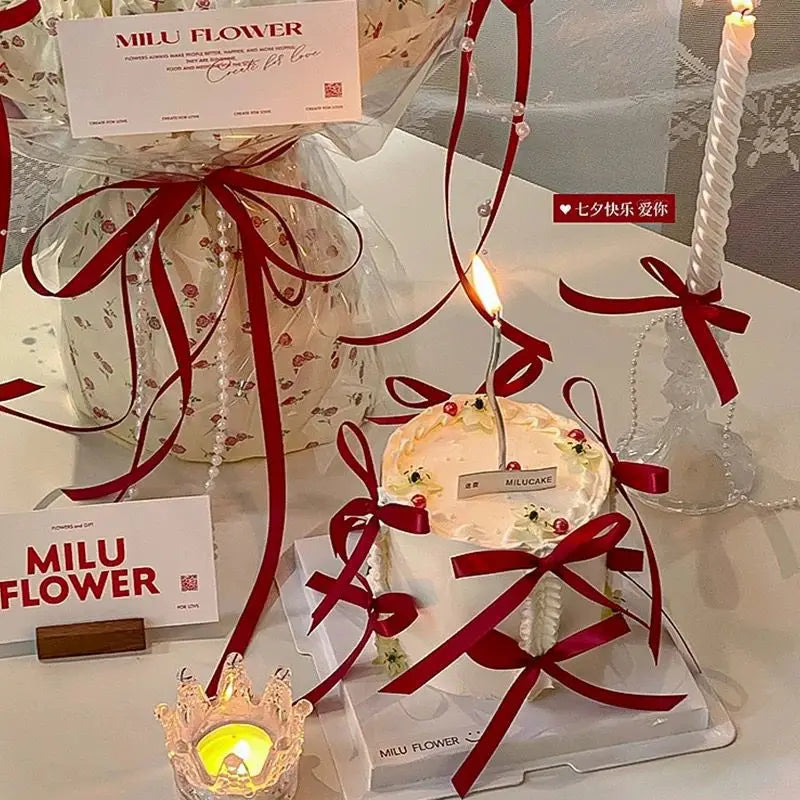 A white cake decorated with flowers and ribbons is displayed on a glass stand.