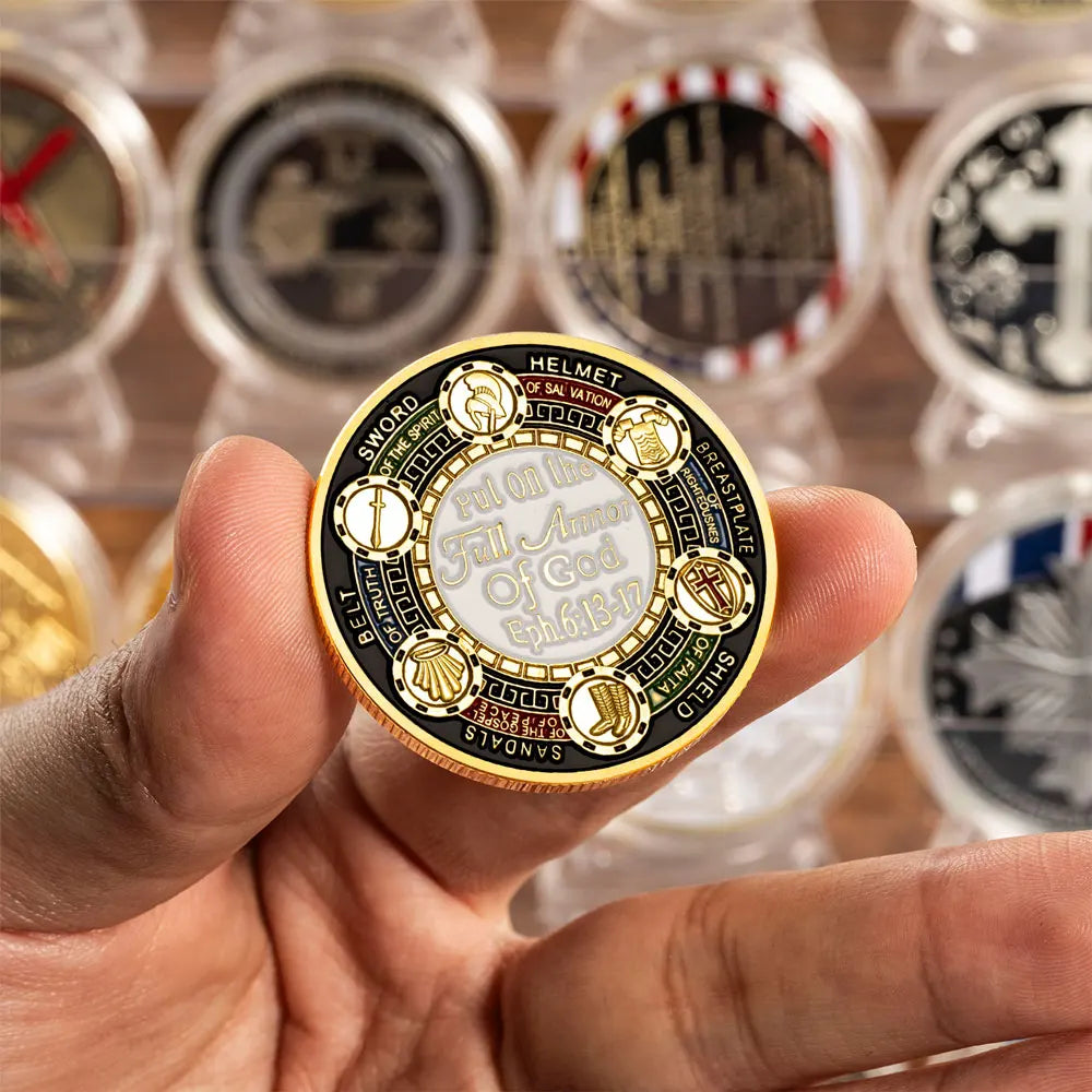 A hand holds a golden plated commemorative coin featuring various symbols of the Armor of God.