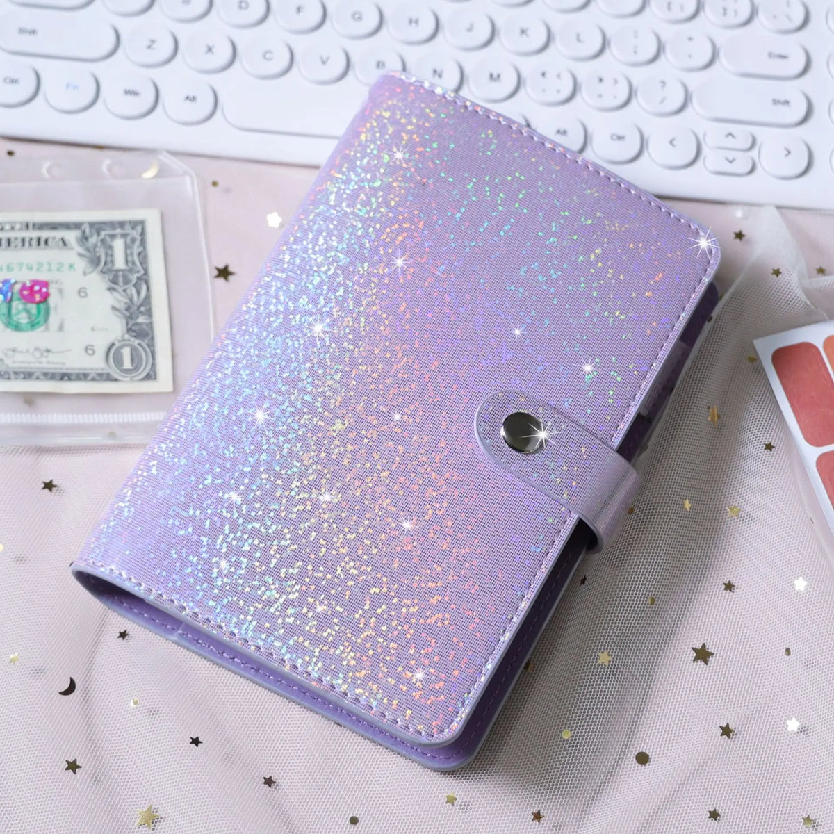 A purple glitter leather cash envelope binder with a silver clasp resting on a pink fabric next to a stack of money.