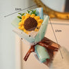A handmade crochet flower bouquet featuring a large yellow sunflower and green foliage, tied with a brown ribbon.