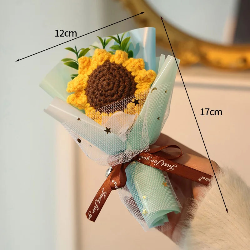 A handmade crochet flower bouquet featuring a large yellow sunflower and green foliage, tied with a brown ribbon.