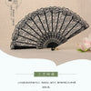A vintage lace folding fan featuring a black and white design, displayed against a beige background.