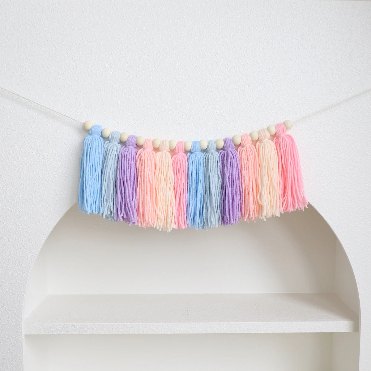 Handmade boho rainbow tassel garland with wooden beads featuring shades of blue, purple, and pink.