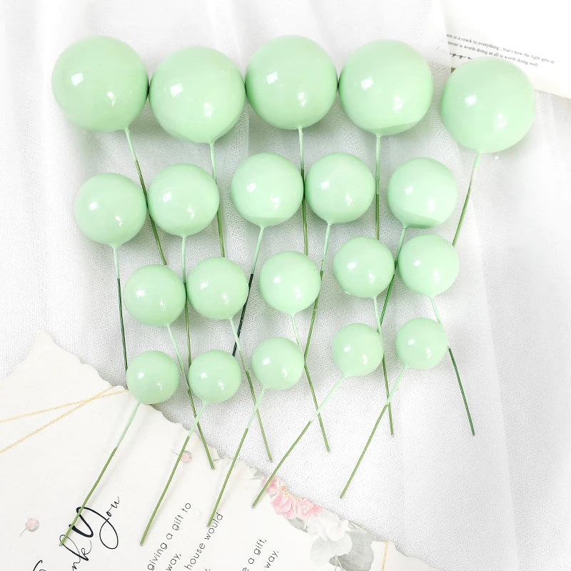 A set of twenty light green spherical ball cake toppers on thin green stems.