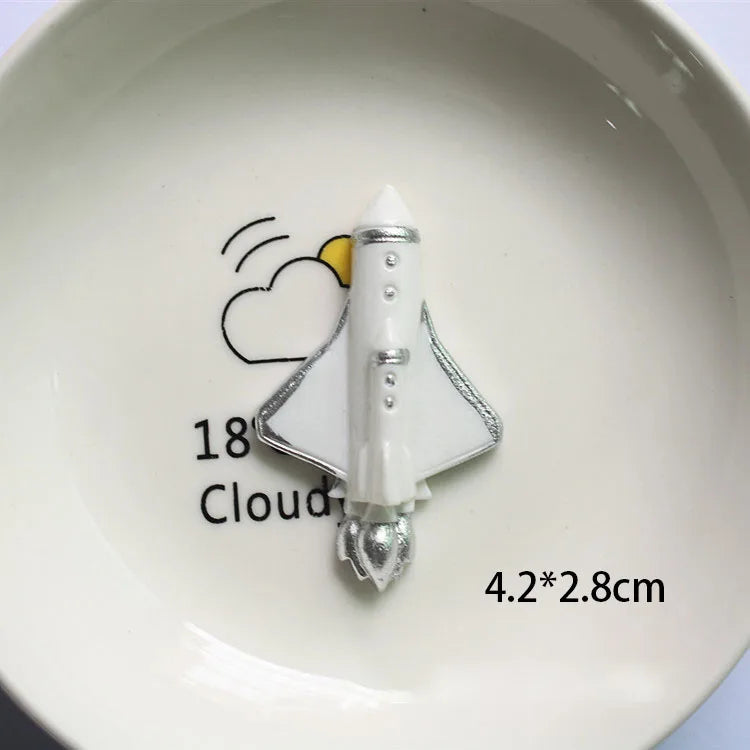 Décoration de gâteau d'astronaute miniature blanche avec accents argentés sur une assiette blanche.