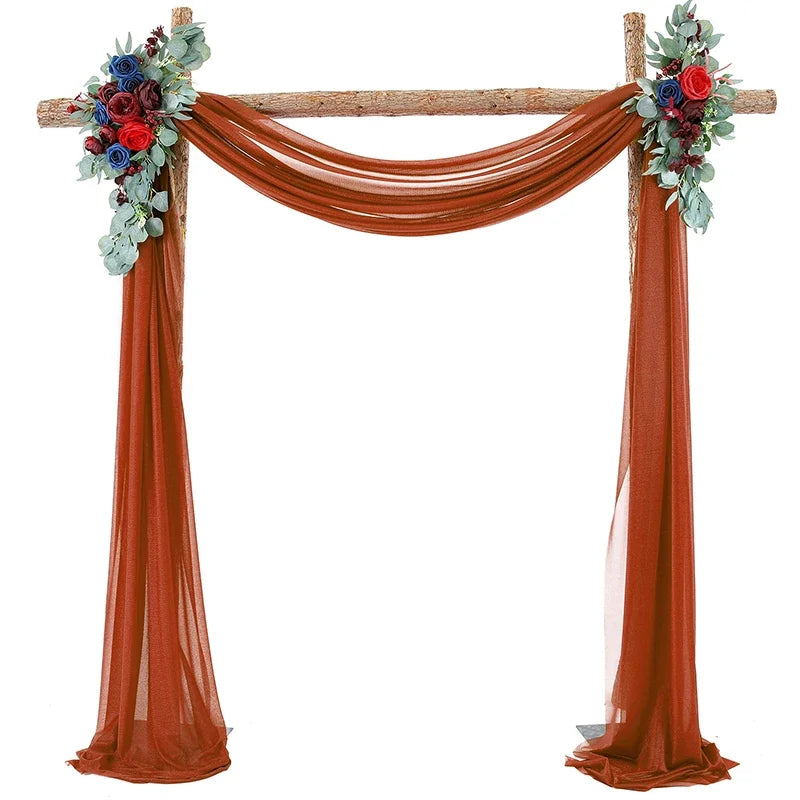 A wooden wedding arch decorated with draping fabric panels in a rust orange color and floral accents.