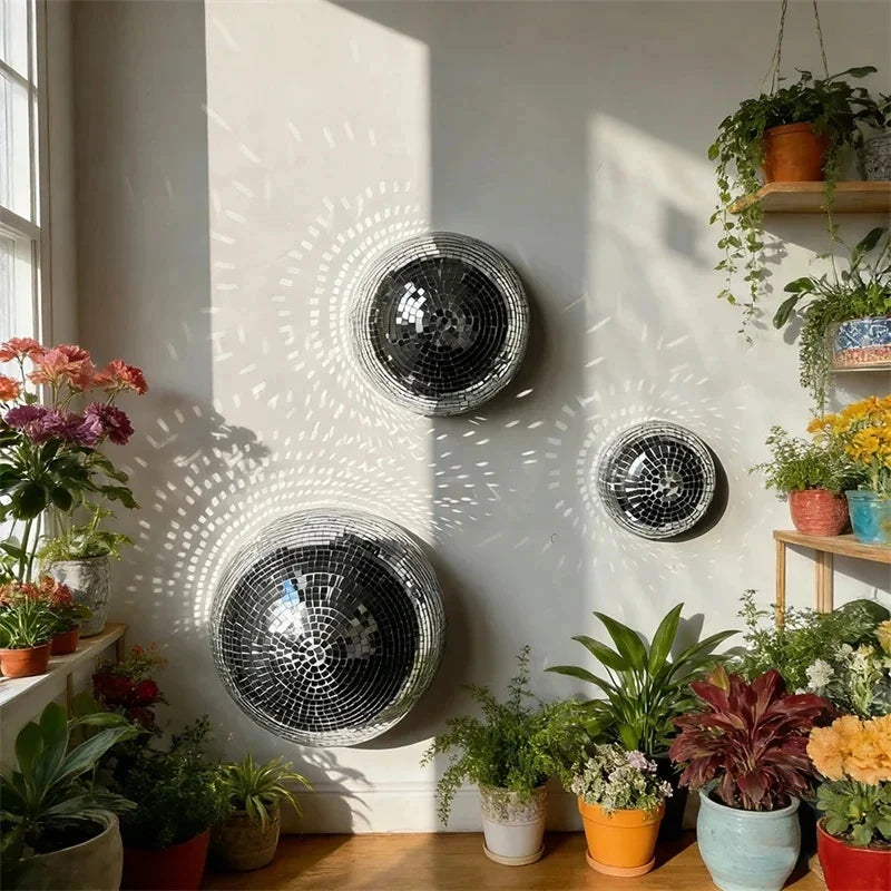 Un miroir décoratif boule disco suspendue sur un mur clair avec des motifs ensoleillés et des plantes en pot