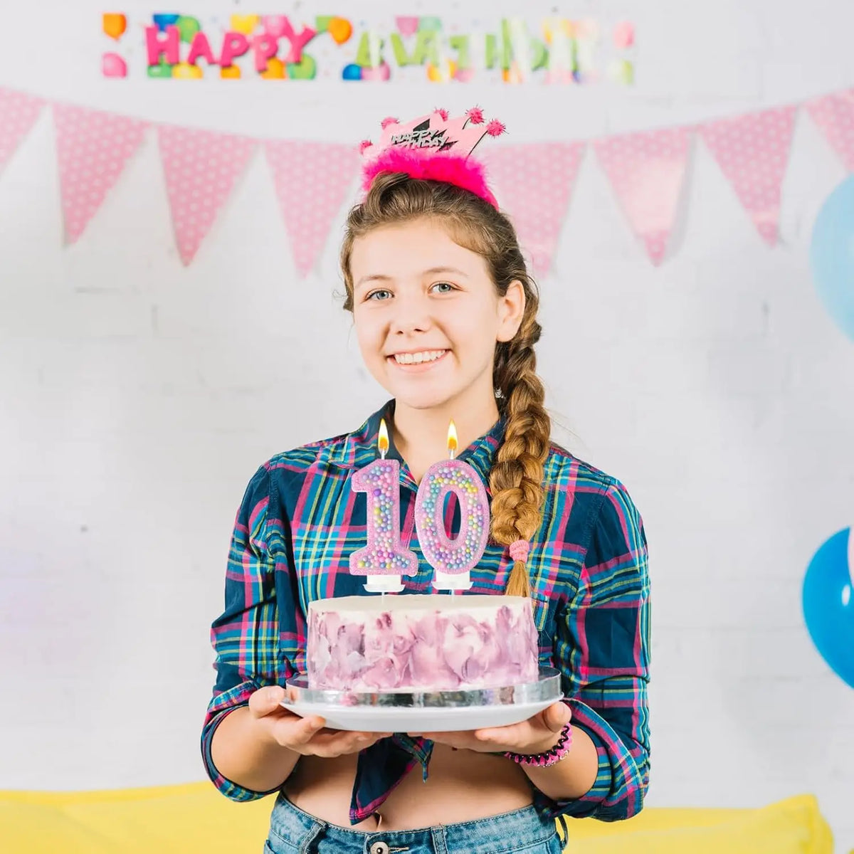 A smiling girl holds a cake decorated with the number 10 candles in front of a pink and white party banner.